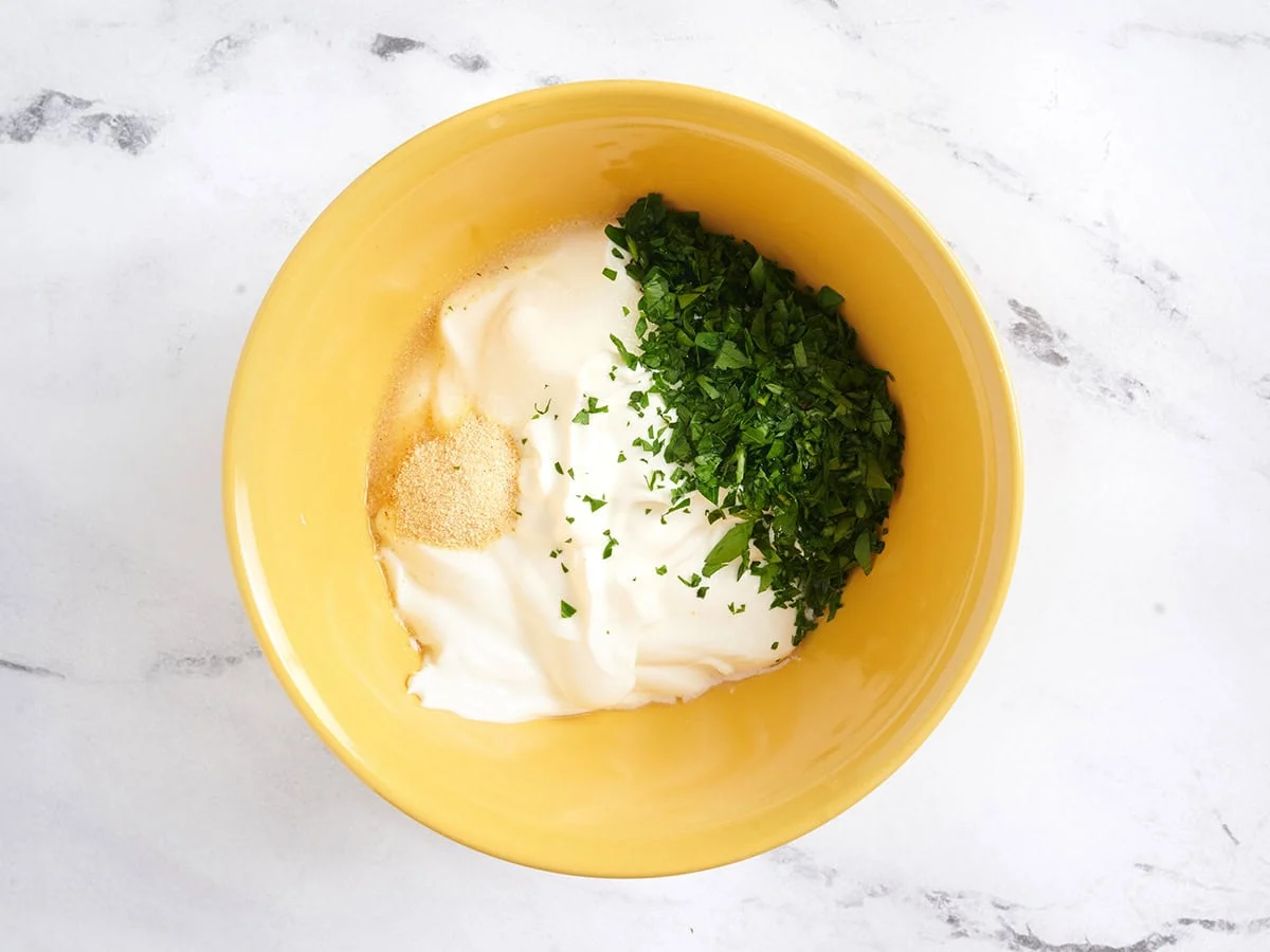 Fresh parsley, garlic powder, and lemon juice added to a bowl of sour cream.
