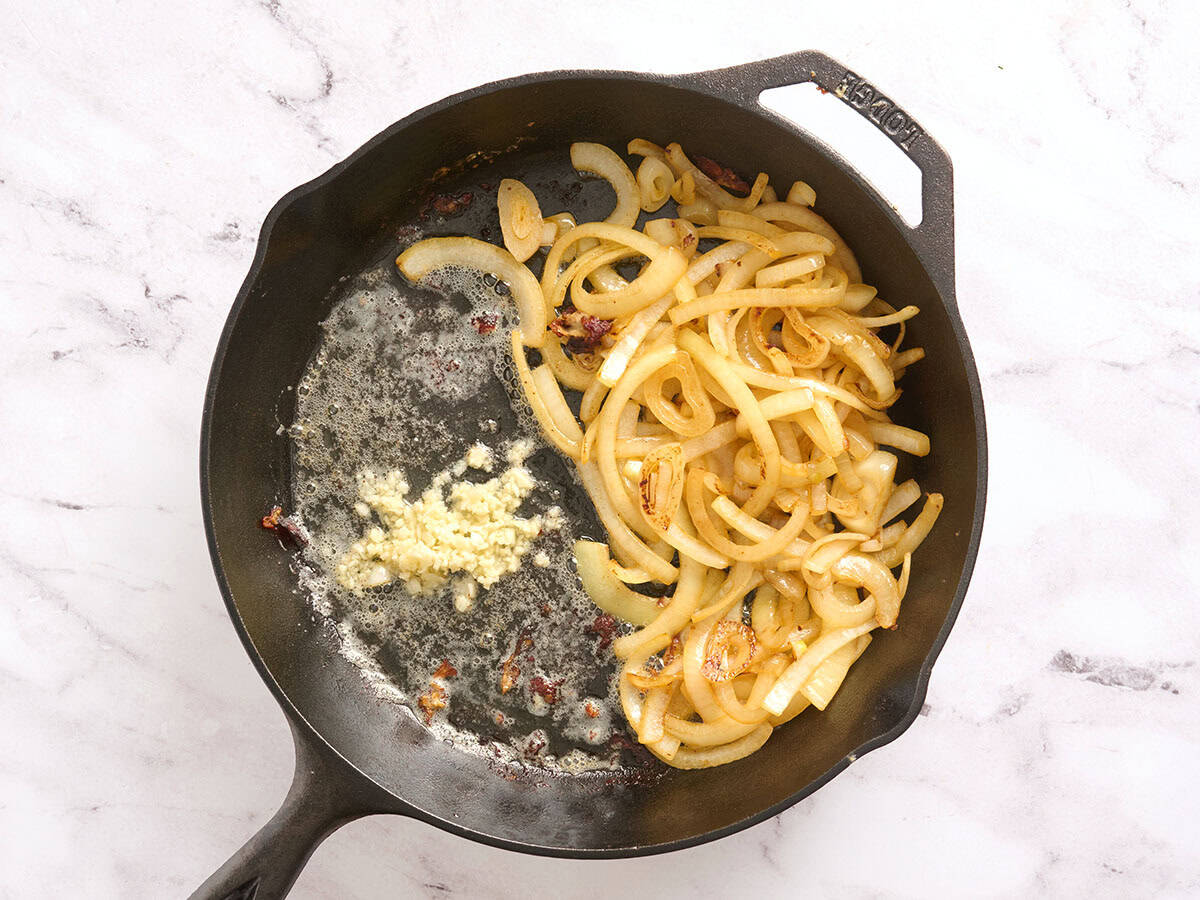Minced garlic and butter added to a skillet with browned onions.