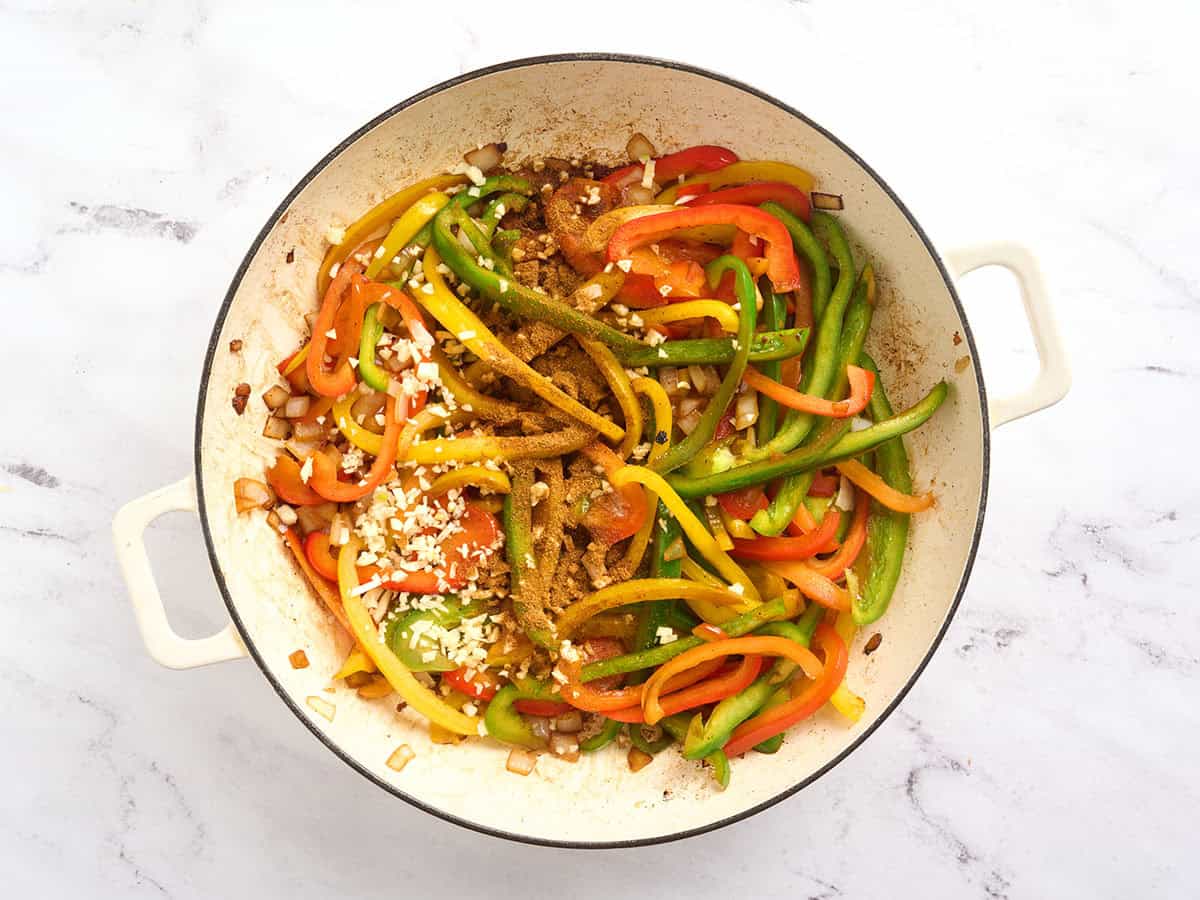 Garlic and jerk seasoning added to a skillet of bell peppers.