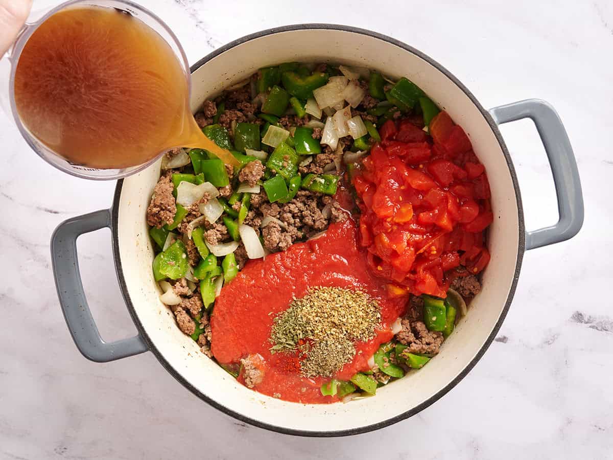 Broth being poured into a pot with diced tomatoes and sauteed veggies.