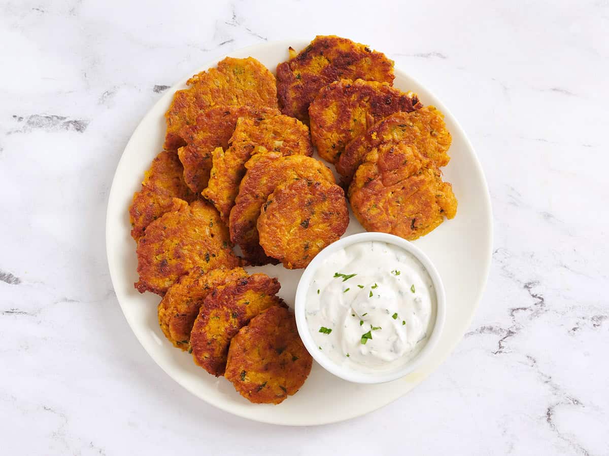 Homemade pumpkin fritters on a plate with a garlic herb dipping sauce.