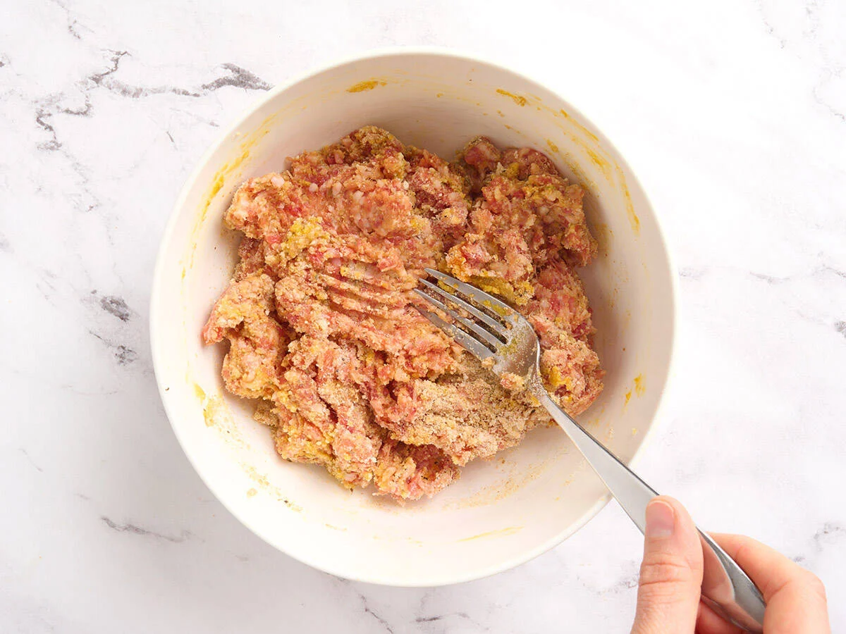 A fork mixing a meatballs mixture in a bowl.