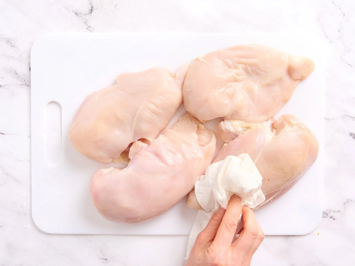A hand patting dry brined chicken breasts.