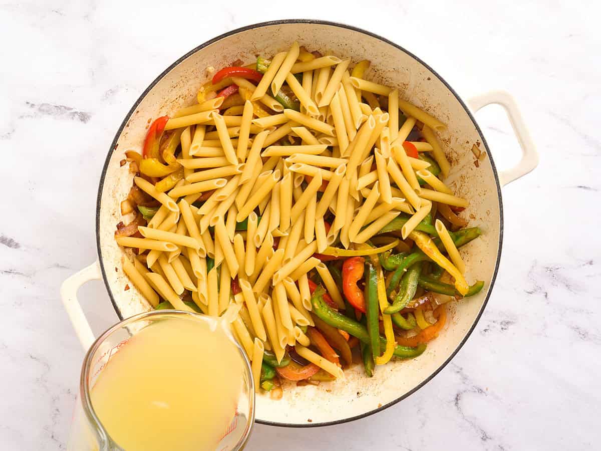 Pasta added to a skillet with bell peppers and chicken broth.