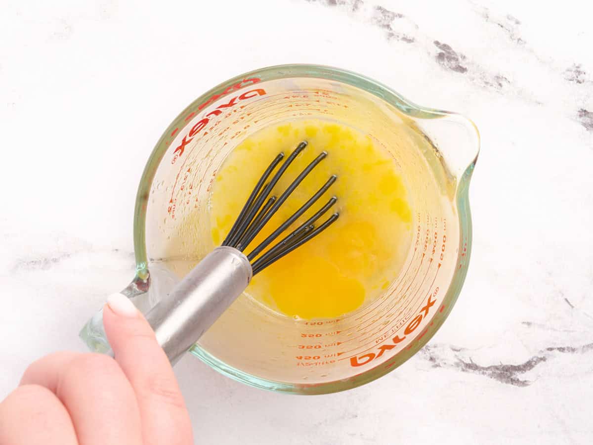 A whisk mixing lemon juice and eggs in a bowl.