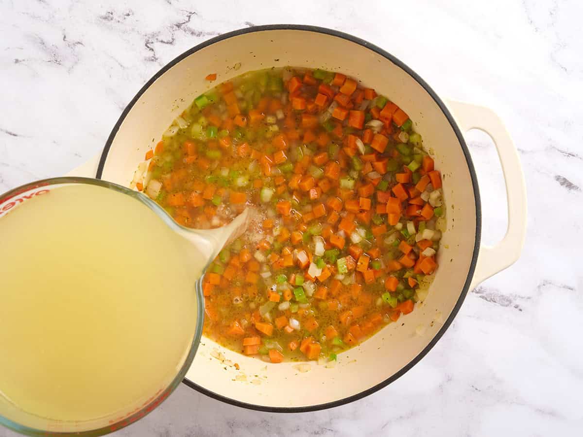 Broth being added to a pot of sauteed veggies.