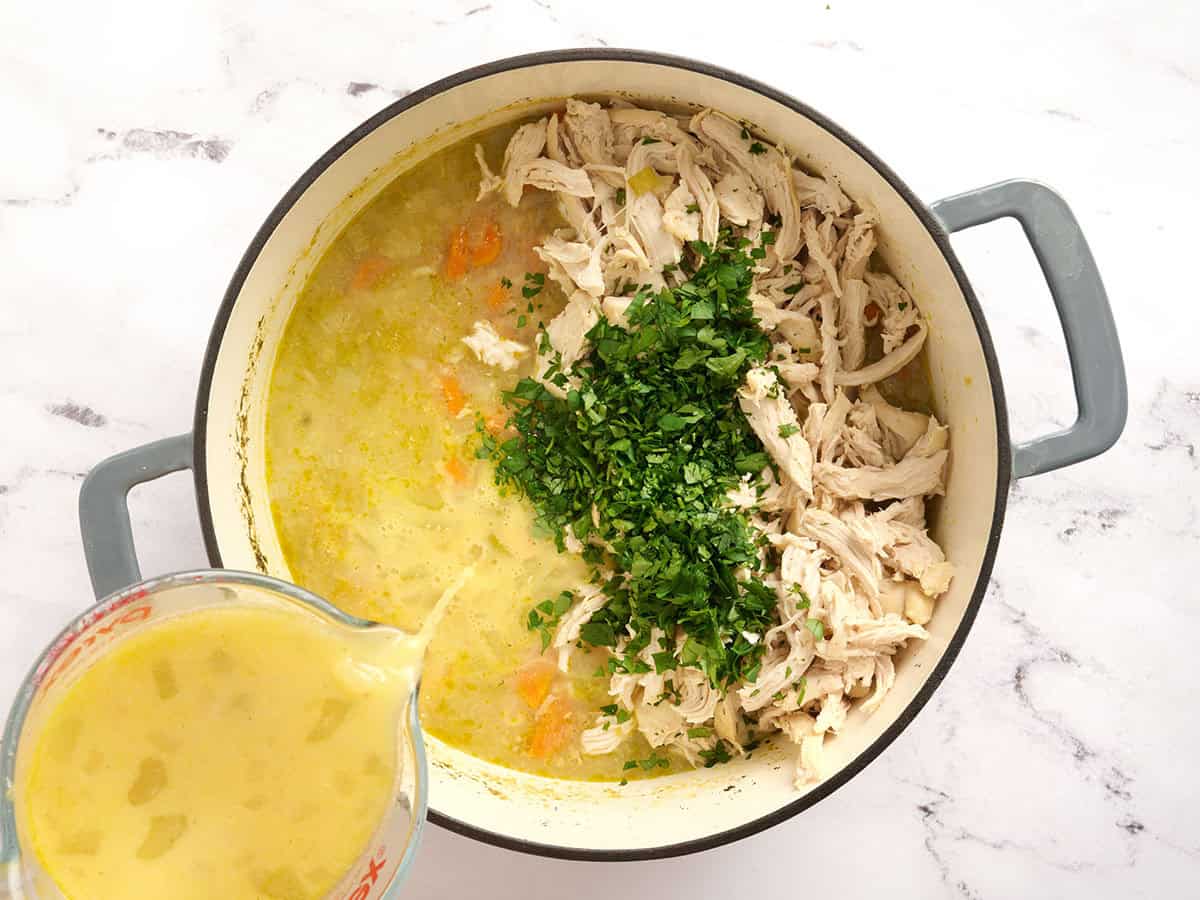 Shredded chicken and parsley added to a pot of soup, with tempered eggs being poured in too.