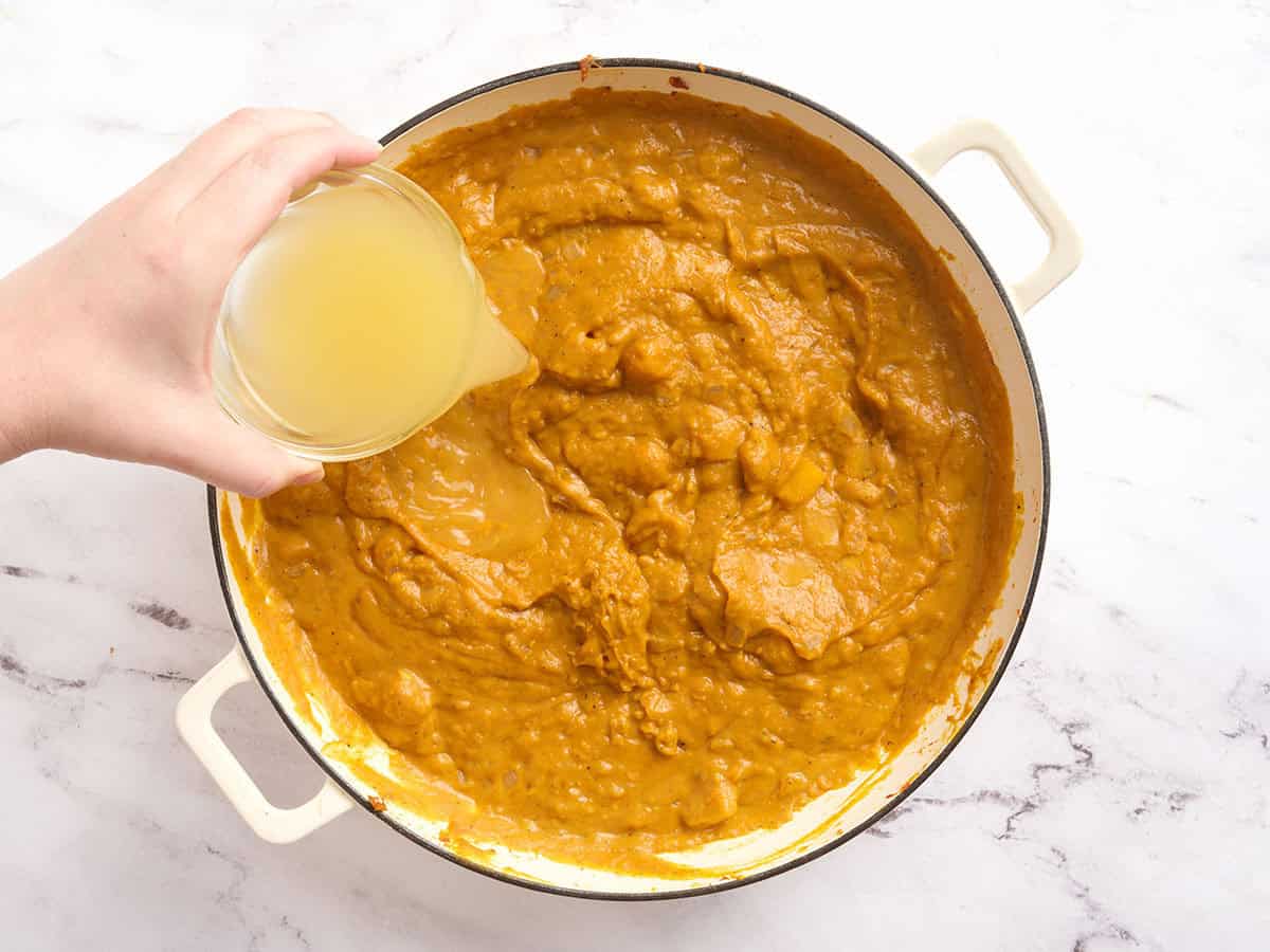 Vegetable broth added to a pot of pumpkin curry.