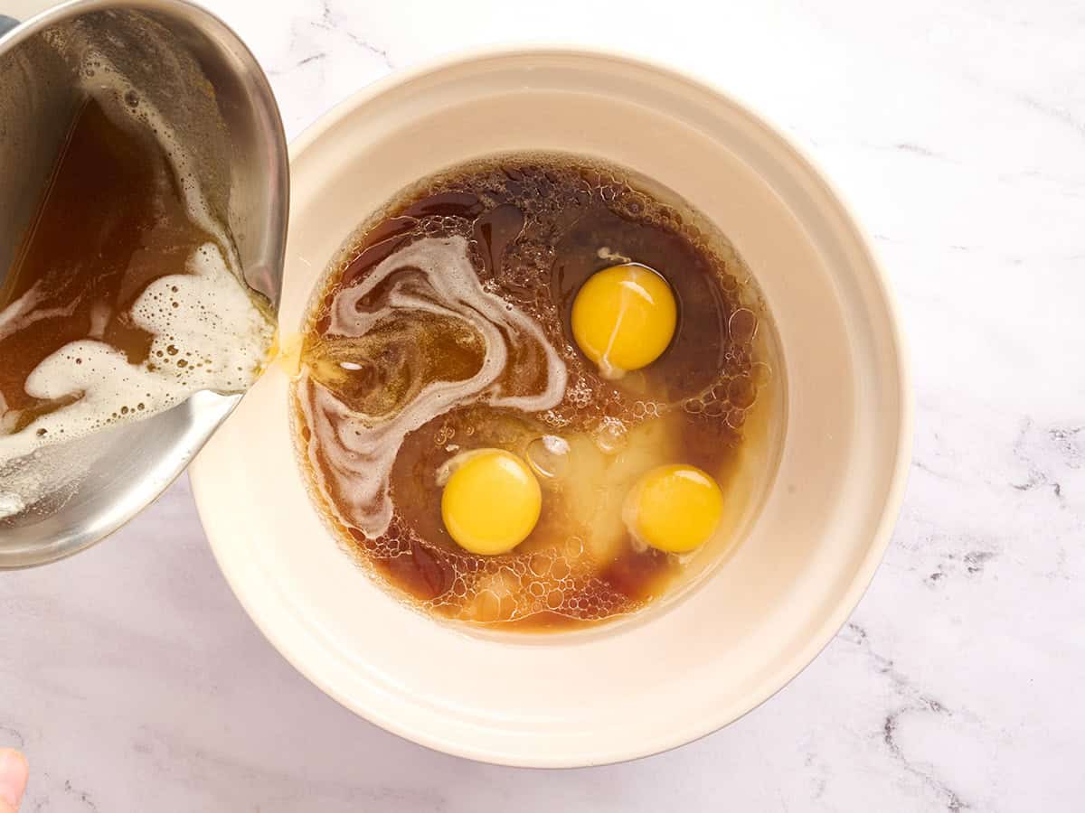 Browned butter being poured into eggs and brown sugar in a mixing bowl.