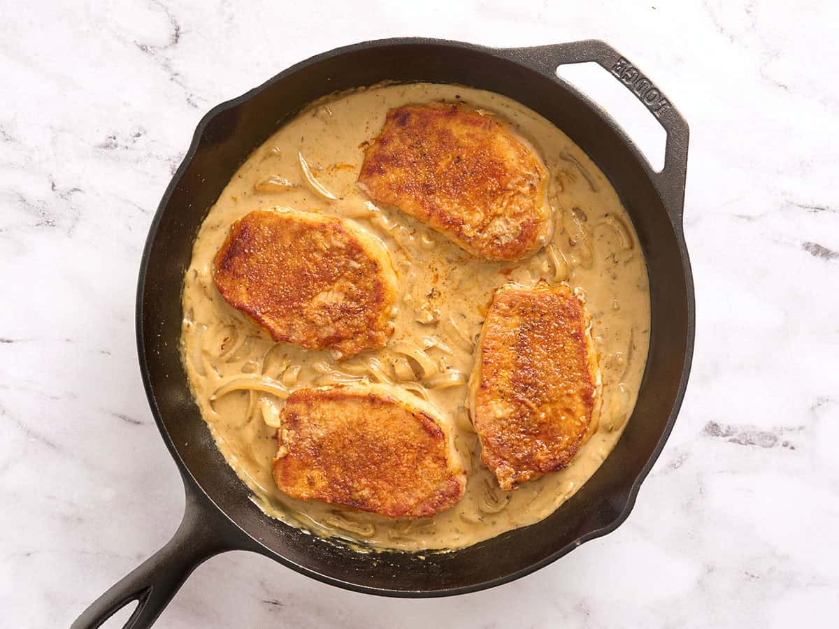 Pork chops added to a skillet with a creamy mushroom sauce.