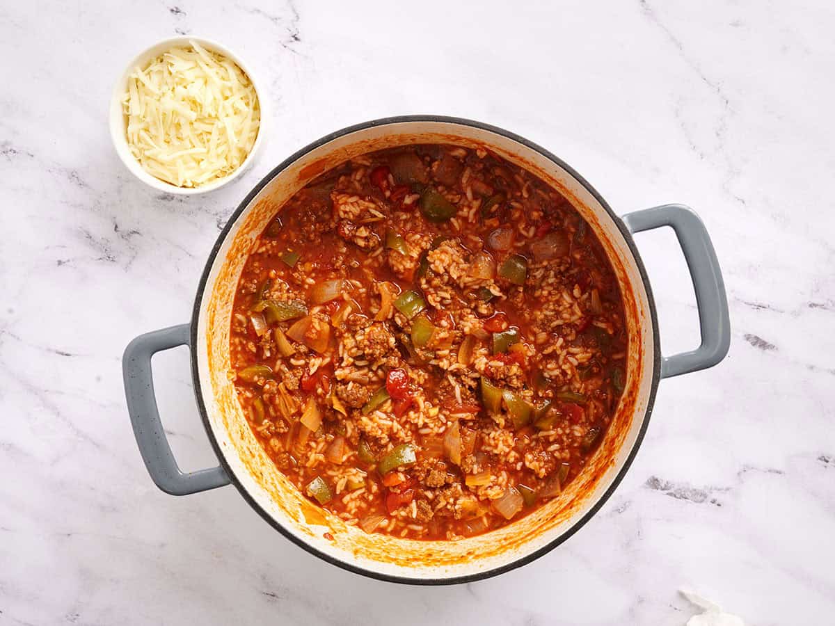 Finished stuffed pepper soup in a pot next to a bowl of shredded cheese.