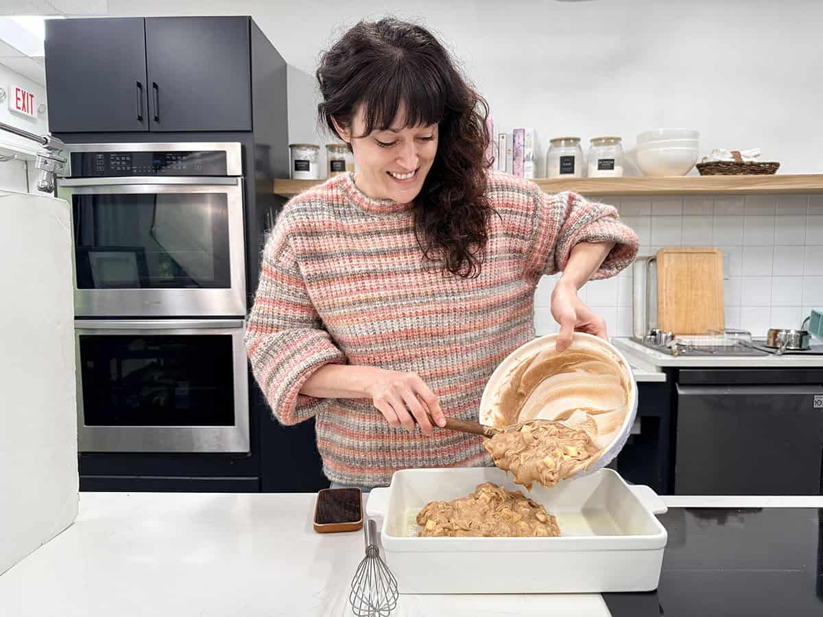 Front view of a women pouring cake batter into a baking dish in a kitchen.