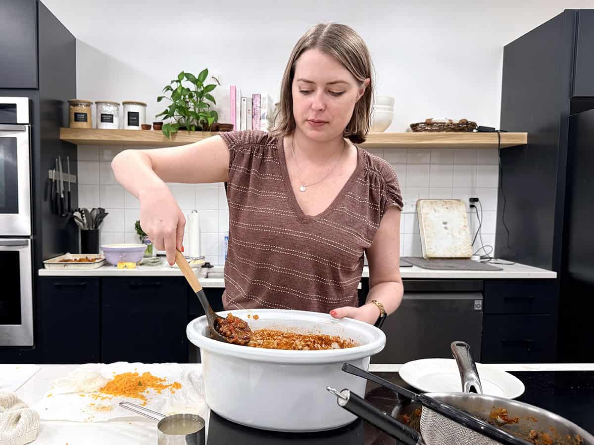 Front view of a women ladling crockpot chili from a slow cooker.