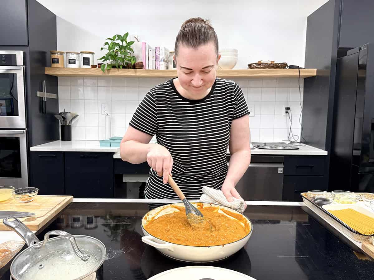 A woman cooking a pumpkin curry on a stovetop in a kitchen.