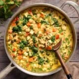 Overhead view of a skillet of coconut curry beans and greens with a wooden spoon.