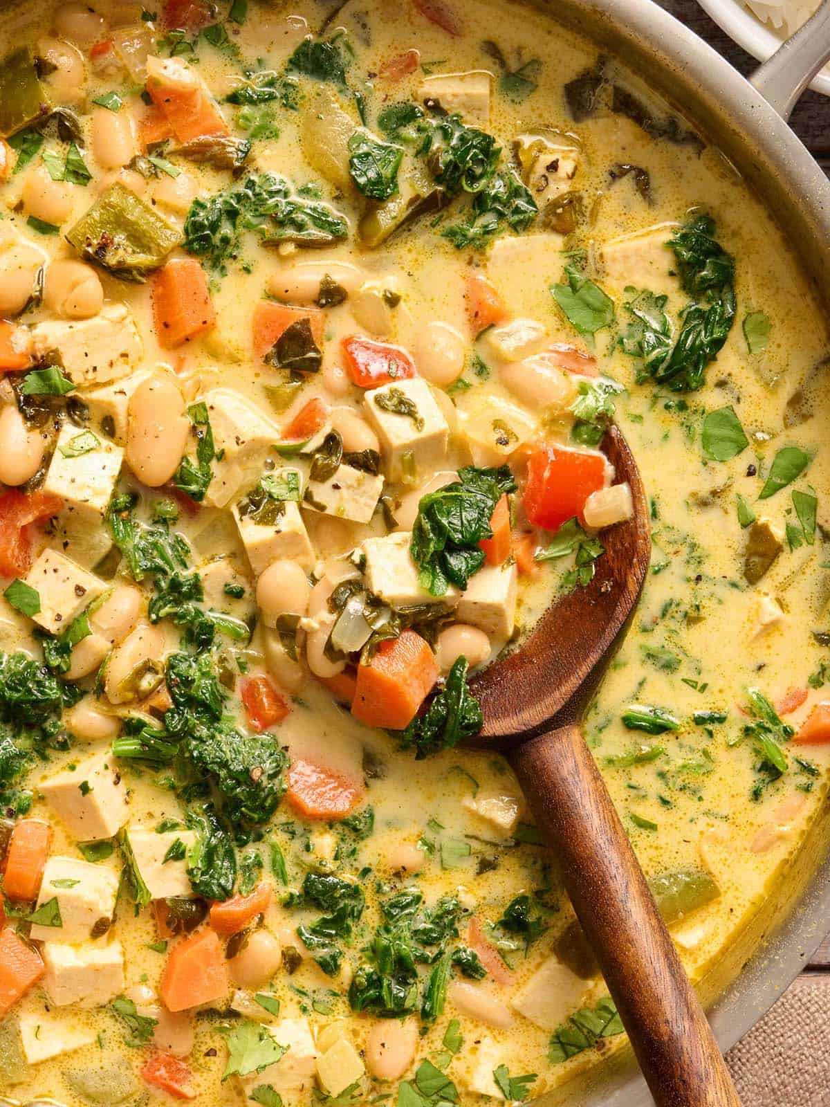 Overhead view of a skillet of coconut curry beans and greens with a wooden spoon.