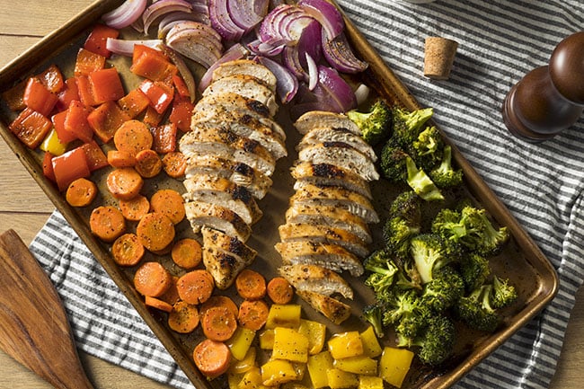Sheet pan supper with roasted chicken, carrots, broccoli, and red onions.