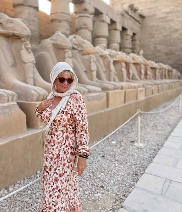 A woman wearing a long dress and white scarf around her head in a temple in Egypt.