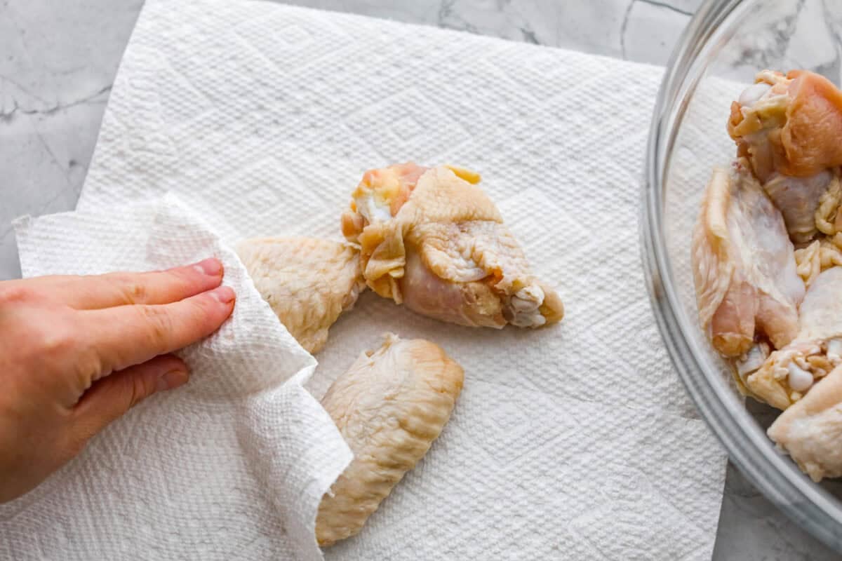 Get ready to get a little messy with these gold fever chicken wings! Baked until crispy and tossed in a sweet, tangy, buttery sauce with a kick of heat, they're perfect for game day, parties, or anytime a wing craving hits! Someone patting the chicken wings dry with paper towels.