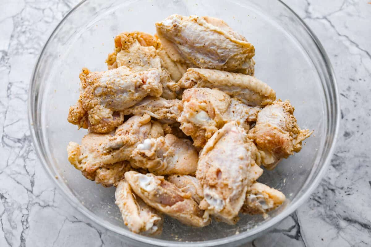 Get ready to get a little messy with these gold fever chicken wings! Baked until crispy and tossed in a sweet, tangy, buttery sauce with a kick of heat, they're perfect for game day, parties, or anytime a wing craving hits! Chicken wings tossed in the bowl and coated in the seasonings.