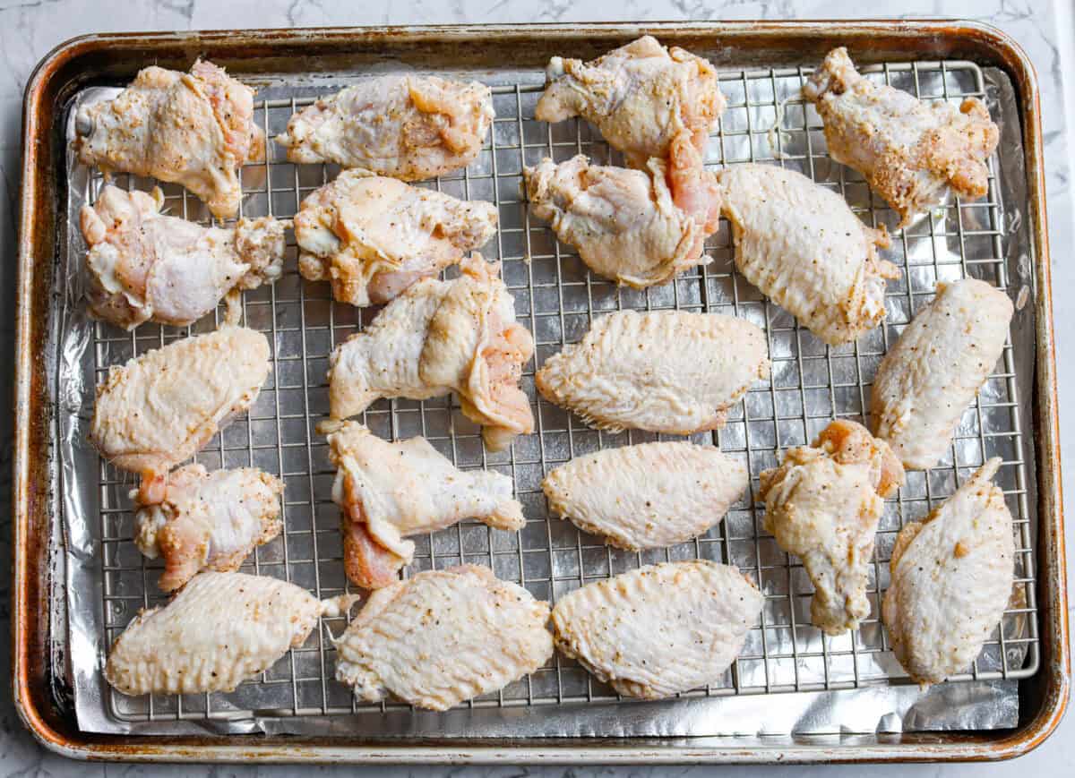 Get ready to get a little messy with these gold fever chicken wings! Baked until crispy and tossed in a sweet, tangy, buttery sauce with a kick of heat, they're perfect for game day, parties, or anytime a wing craving hits! Seasoned chicken wings spread out on a cooling wrack that is placed over a foil lined baking sheet.