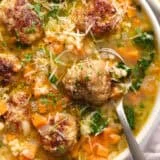 Overhead close up view of a bowl of Italian wedding soup with a spoon.