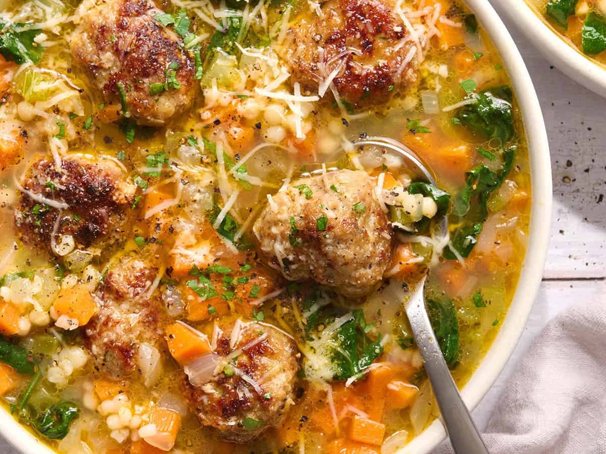 Overhead close up view of a bowl of Italian wedding soup with a spoon.