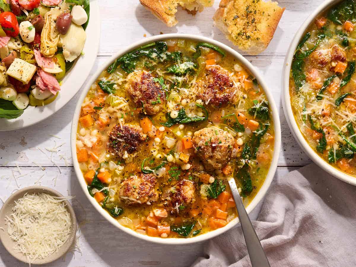 Overhead view of Italian wedding soup in a bowl with a side salad, shredded parmesan and garlic bread.
