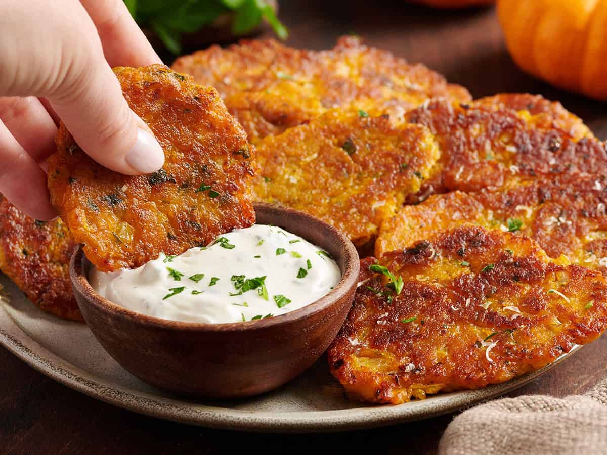 A pumpkin fritter being dipped into a garlic herb dip.