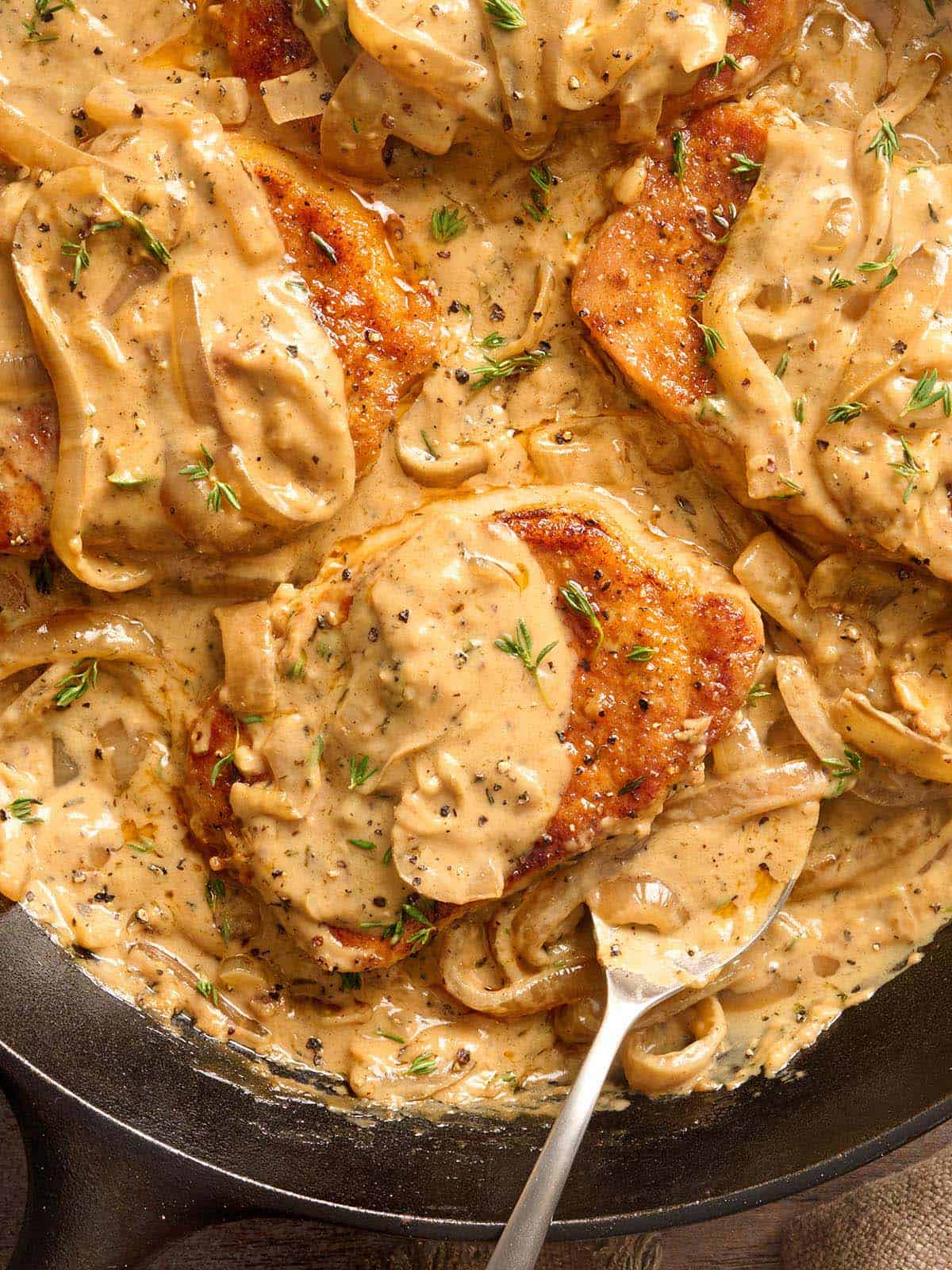 Close up view of smothered pork chops in a skillet with a spoon.