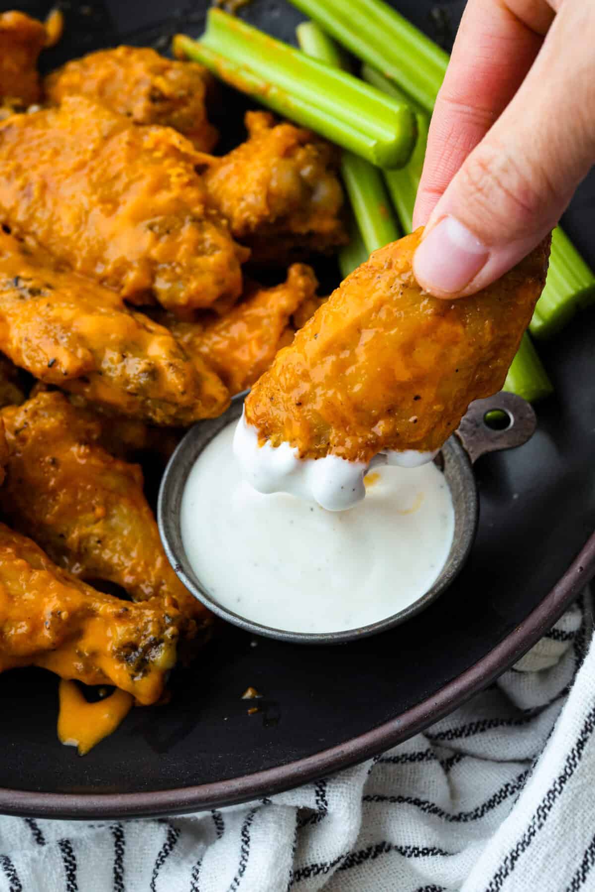 Get ready to get a little messy with these gold fever chicken wings! Baked until crispy and tossed in a sweet, tangy, buttery sauce with a kick of heat, they're perfect for game day, parties, or anytime a wing craving hits! Someone dipping a chicken wing into the ranch dressing.